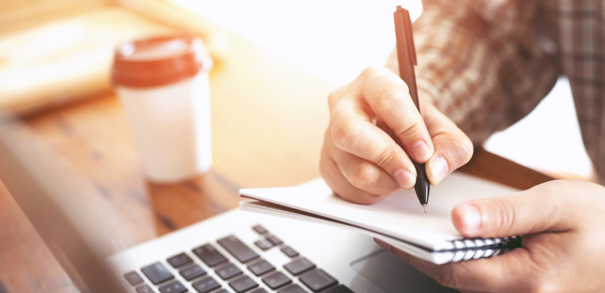 person taking notes near a laptop