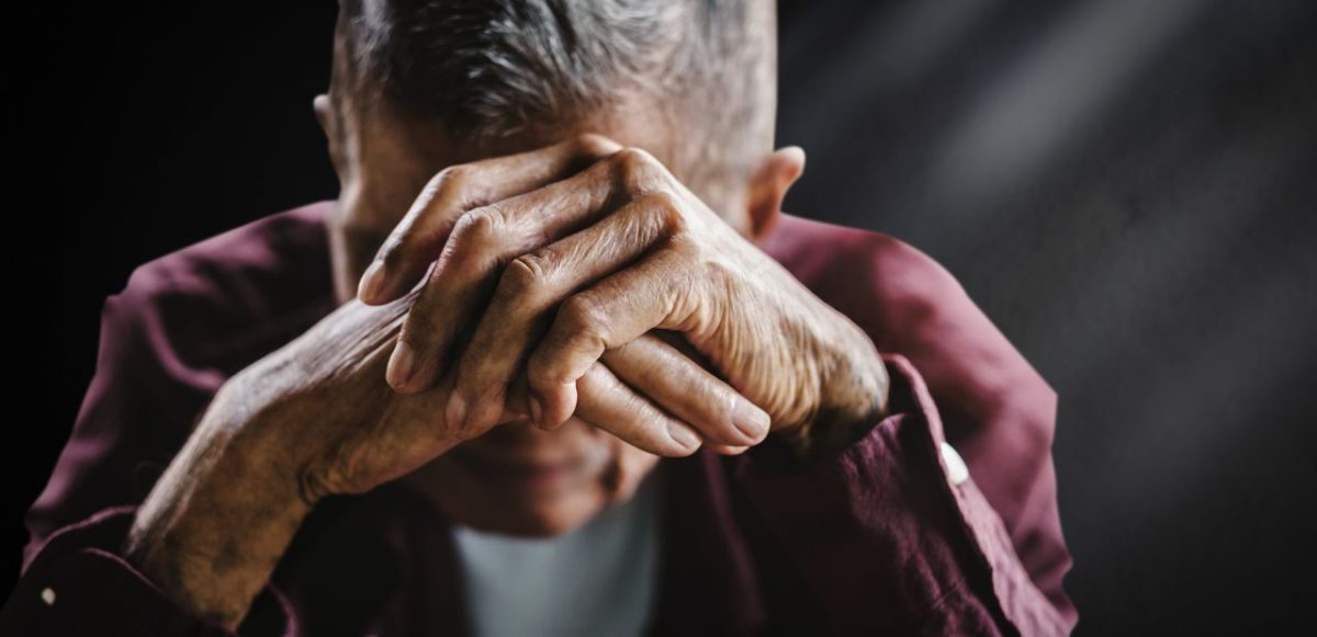 Senior man holding hands in front of face.