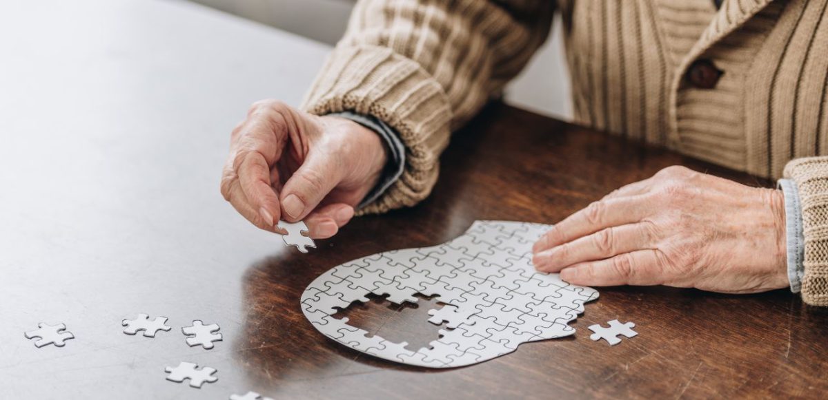 Senior assembling a jigsaw puzzle shaped like a human head silhouette.