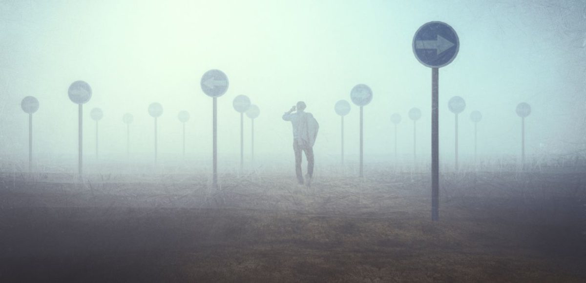 A fog filled landscape, dotted with conflicting arrow signs. A man in the middle looks lost.