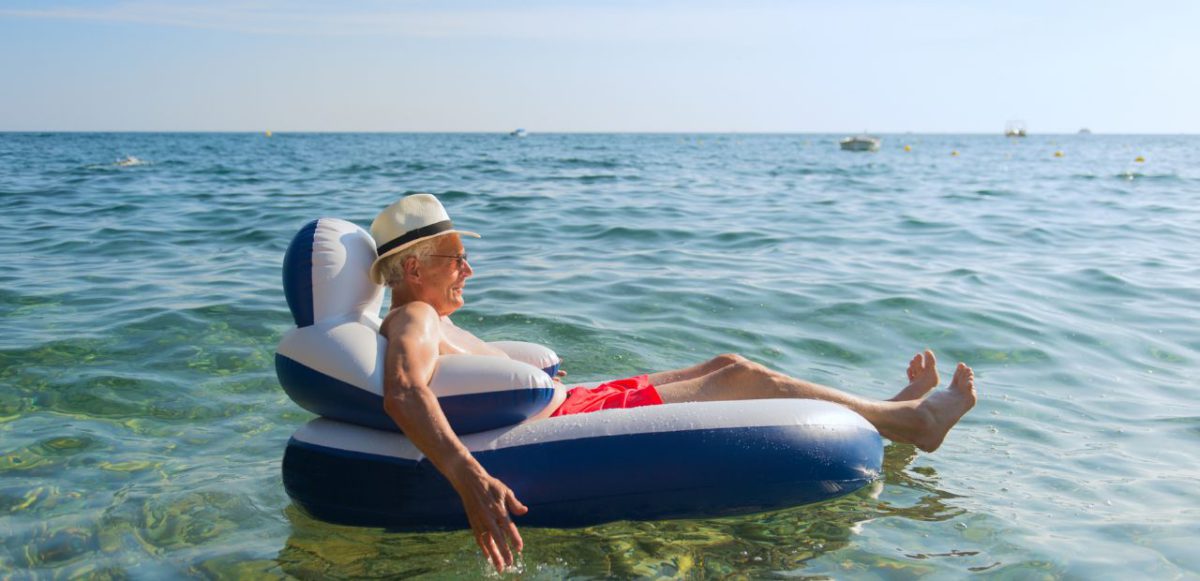 Senior floating on inflatable lounge in ocean.