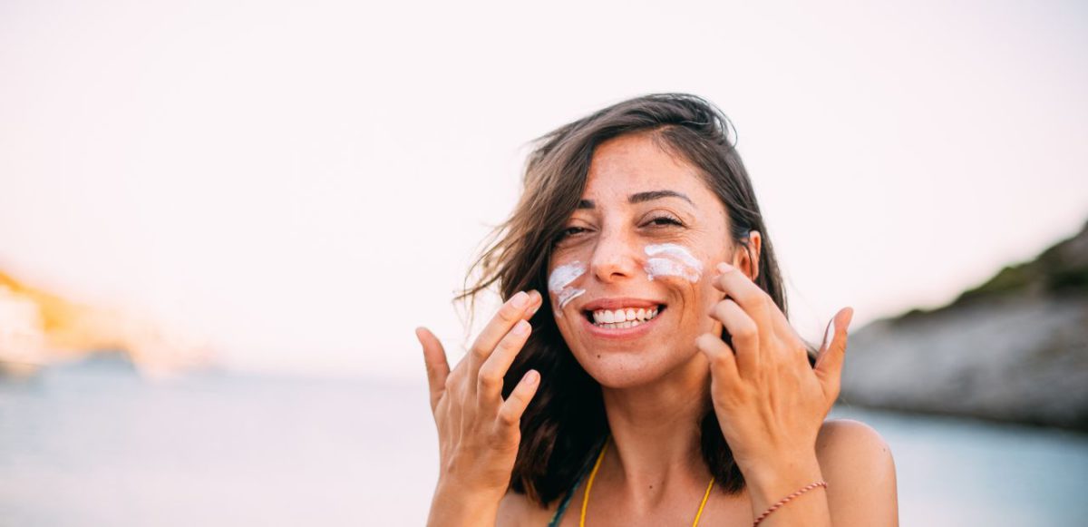A woman applying sunscreen to her face.